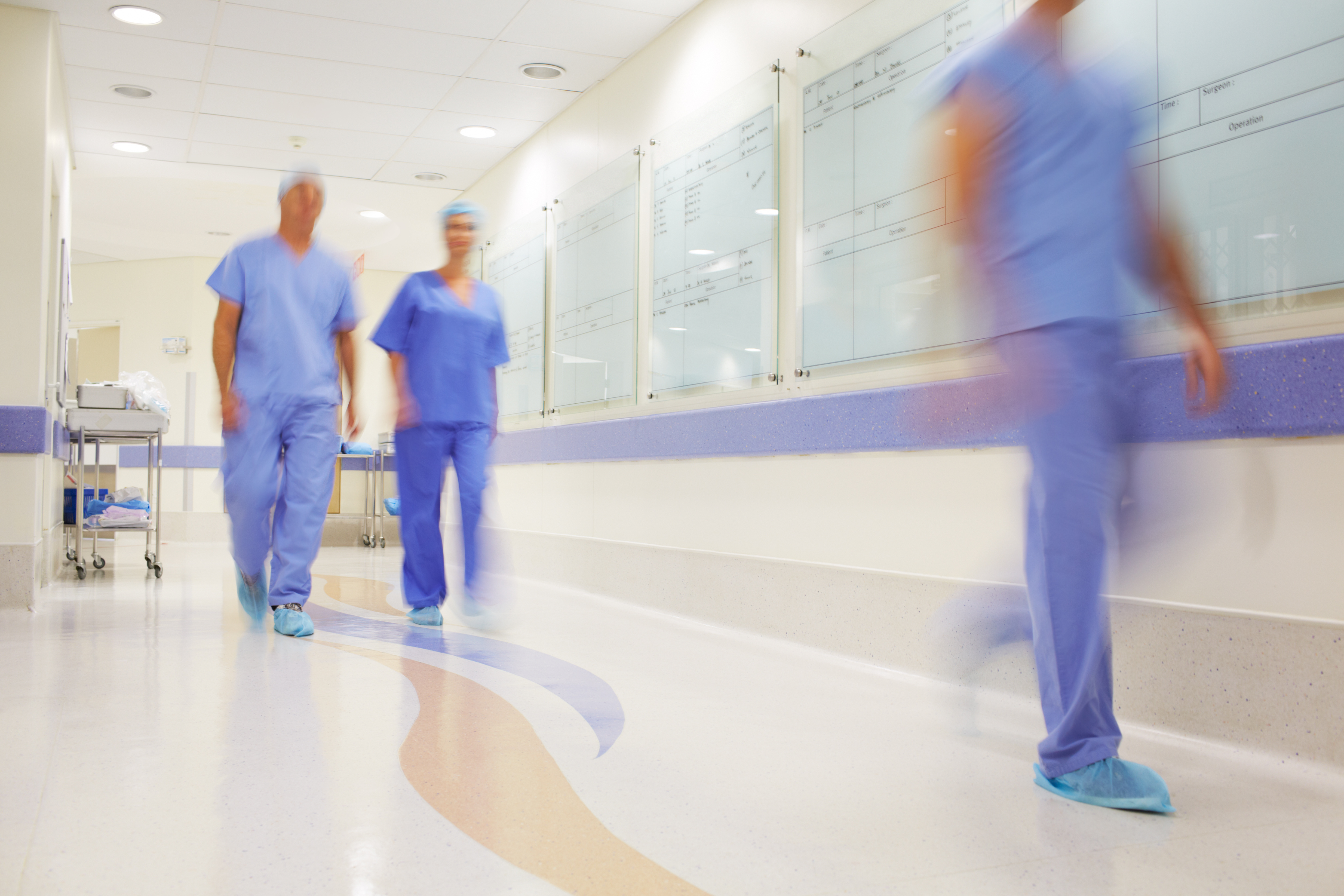 Hospital staff in scrubs walking along a hospital corridor.